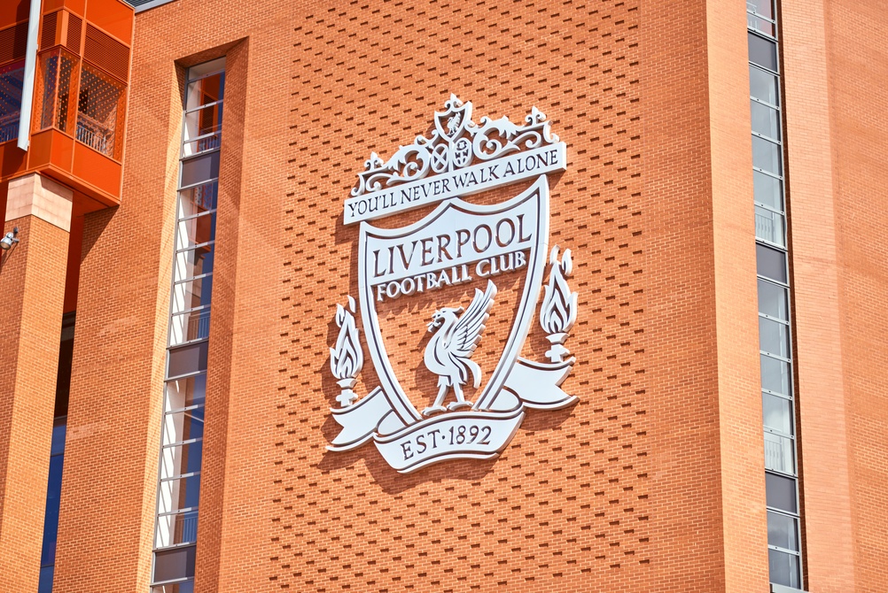 The white Liverpool Football Club crest on the red brick exterior wall of Anfield Stadium